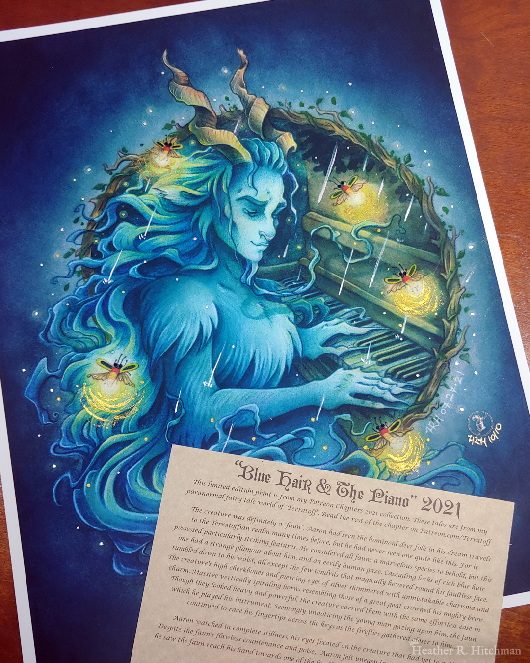 Photograph of a watercolor and gouache painting print of a blue faun playing piano in a light rain. The faun sits at a ¾ angle, with a tranquil expression while looking down at his hands playing the keys below. Fireflies fly around him and illuminate the dark blue scene. A circular hoop of branches frames the faun and piano from the waist up, leaving only a portion of the top of the piano visible. The faun appears to be leaning towards the viewer with his torso slightly exiting the frame of branches. His long blue hair and twisting goat horns protrude outside of the branch frame, creating a feeling of depth and three dimensional space. Watercolor paints and brushes are placed on top of the painting across the bottom right. The print has a ¼ inch white border and is laying on top of a wooden backdrop. The fireflies have small sparkling black crystals for eyes, and their light has been embellished with golden paint. The rain has been painted with silver paint and is catching the light brightly. A piece of parchment paper with a story printed on it lays over top of the bottom of the print.