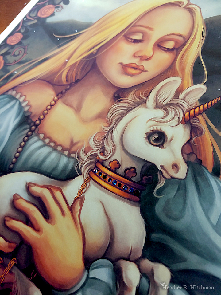 Close up photograph of print of a digital portrait painting of a woman holding a baby unicorn in her arms. The woman has long flowing blond hair, and wears a medieval gown of light blue with puffy sleeves and an off the shoulder neckline. The woman looks young, and wears a white pearl necklace. She is facing forward, holding the unicorn towards the right. She looks down with an adoring expression through partially closed eyes. The white unicorn she holds to her chest is a foal, with large black eyes, a small golden horn, and large upright ears. The unicorn has a happy expression on its face, and wears a golden crown around its neck with a gold chain attached that is wrapped around one of the woman’s hands. In the background is a daytime landscape scene of rolling green hills and a border of roses. The photo is taken at an angle, and focuses on the small red and blue swarovski crystals that have been adhered to the print across the band of the unicorn’s crown.