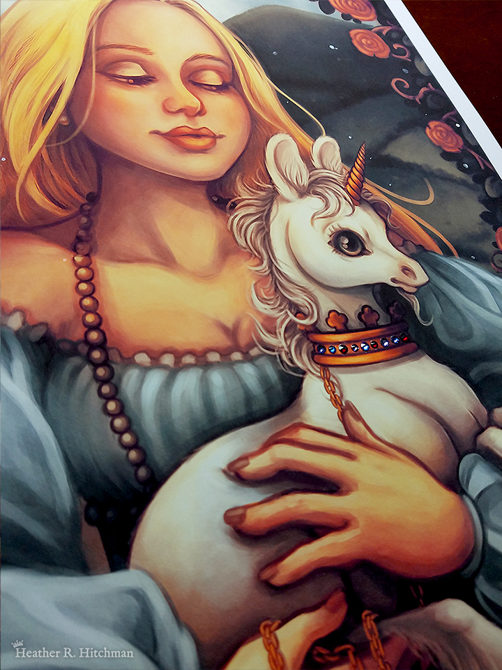 Close up photograph of print of a digital portrait painting of a woman holding a baby unicorn in her arms. The woman has long flowing blond hair, and wears a medieval gown of light blue with puffy sleeves and an off the shoulder neckline. The woman looks young, and wears a white pearl necklace. She is facing forward, holding the unicorn towards the right. She looks down with an adoring expression through partially closed eyes. The white unicorn she holds to her chest is a foal, with large black eyes, a small golden horn, and large upright ears. The unicorn has a happy expression on its face, and wears a golden crown around its neck with a gold chain attached that is wrapped around one of the woman’s hands. In the background is a daytime landscape scene of rolling green hills and a border of roses. The photo is taken at an angle, and focuses on the small red and blue swarovski crystals that have been adhered to the print across the band of the unicorn’s crown.