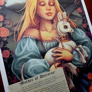 Photograph of a print of a mid leg up digital portrait painting of a woman holding a baby unicorn in her arms. The woman has long flowing blond hair, and wears a medieval gown of light blue with puffy sleeves and an off the shoulder neckline. The woman looks young, and wears a white pearl necklace that flows down to her skirt. She is facing forward, holding the unicorn towards the right. She looks down with an adoring expression through partially closed eyes. The white unicorn she holds to her chest is a foal, with large black eyes, a small golden horn, and large upright ears. The unicorn has a happy expression on its face, and wears a golden crown around its neck with a gold chain attached that is wrapped around one of the woman’s hands. In the background is a daytime landscape scene of rolling green hills. A border of leaves filled with red roses and twisting vines encircles the edges of the scene, arching high above the woman’s head and flowing down the sides partially covering the sides of her dress. The print has a ½ inch white border around the edges, and rests against a wooden art table. A sepia parchment paper with a story written on it is placed over top of the left corner of the print.