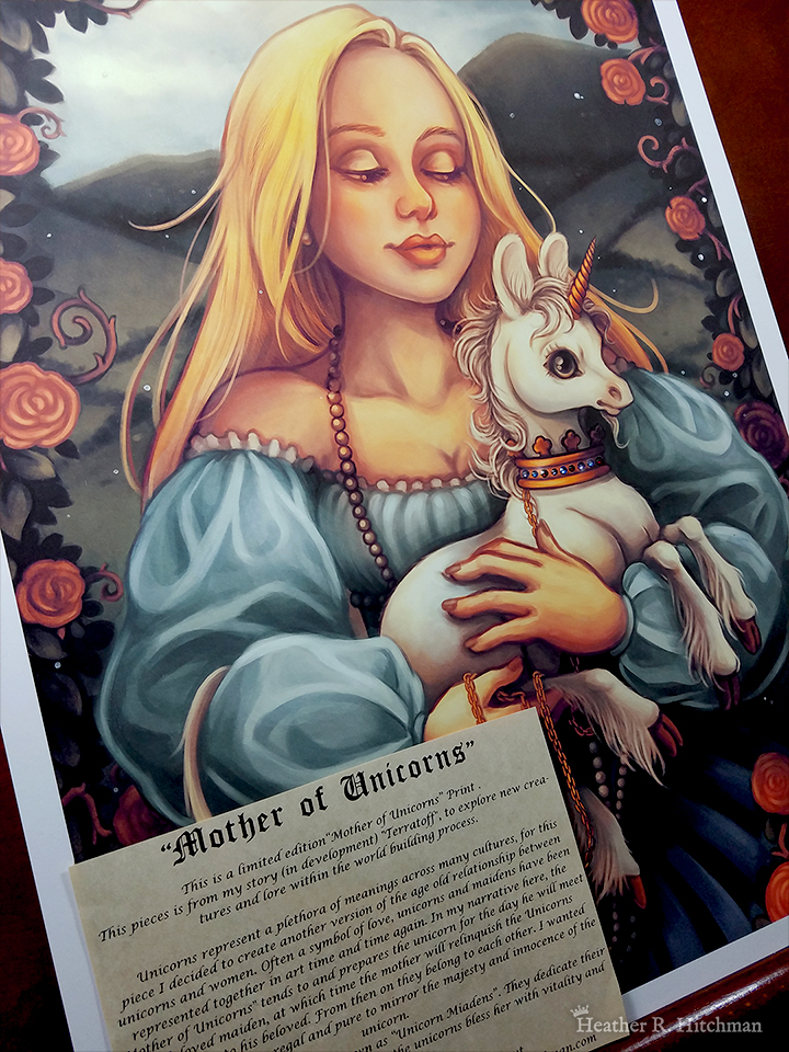 Photograph of a print of a mid leg up digital portrait painting of a woman holding a baby unicorn in her arms. The woman has long flowing blond hair, and wears a medieval gown of light blue with puffy sleeves and an off the shoulder neckline. The woman looks young, and wears a white pearl necklace that flows down to her skirt. She is facing forward, holding the unicorn towards the right. She looks down with an adoring expression through partially closed eyes. The white unicorn she holds to her chest is a foal, with large black eyes, a small golden horn, and large upright ears. The unicorn has a happy expression on its face, and wears a golden crown around its neck with a gold chain attached that is wrapped around one of the woman’s hands. In the background is a daytime landscape scene of rolling green hills. A border of leaves filled with red roses and twisting vines encircles the edges of the scene, arching high above the woman’s head and flowing down the sides partially covering the sides of her dress. The print has a ½ inch white border around the edges, and rests against a wooden art table. A sepia parchment paper with a story written on it is placed over top of the left corner of the print.