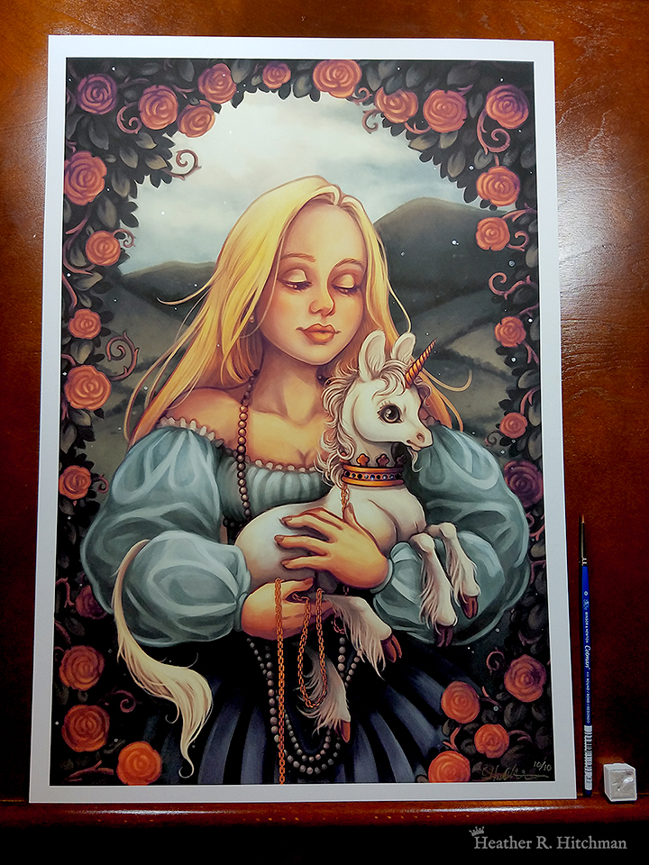 Photograph of a print of a mid leg up digital portrait painting of a woman holding a baby unicorn in her arms. The woman has long flowing blond hair, and wears a medieval gown of light blue with puffy sleeves and an off the shoulder neckline. The woman looks young, and wears a white pearl necklace that flows down to her skirt. She is facing forward, holding the unicorn towards the right. She looks down with an adoring expression through partially closed eyes. The white unicorn she holds to her chest is a foal, with large black eyes, a small golden horn, and large upright ears. The unicorn has a happy expression on its face, and wears a golden crown around its neck with a gold chain attached that is wrapped around one of the woman’s hands. In the background is a daytime landscape scene of rolling green hills. A border of leaves filled with red roses and twisting vines encircles the edges of the scene, arching high above the woman’s head and flowing down the sides partially covering the sides of her dress. The print has a ½ inch white border around the edges, and rests against a wooden art table. To the right of the print is a watercolor paint brush and a small pot of silver pigment.