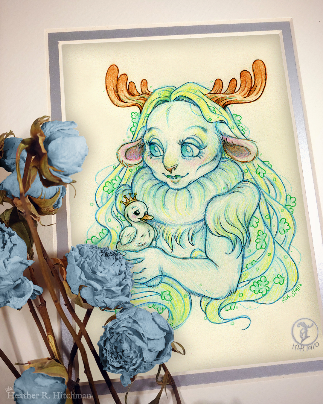 Photograph of a matted print of a graphite and colored pencil chest up portrait drawing of a child female faun with soft blueish green fur, large blue eyes, and small moose antlers. The faun’s fur is gathered into a poofy collar around her neck, creating the illusion of a ruff. The fur gathered at her shoulders looks similar to shoulder pads. She is posing at a ¾ angle to the left holding a tiny swan gosling in her hands. The gosling is wearing a tiny gold crown on its head and is looking up at the faun adoringly. The faun looks back down at the gosling, blushing with a smile on her face. Her long straight blond hair cascades around her back and shoulders, decorated with small green fern leaves. The mat-board is white on the top layer and silver on the second layer. Blue roses rest on top of the print to the left. A small silver stamp with the Terratoff icon is at the bottom right corner of the print.