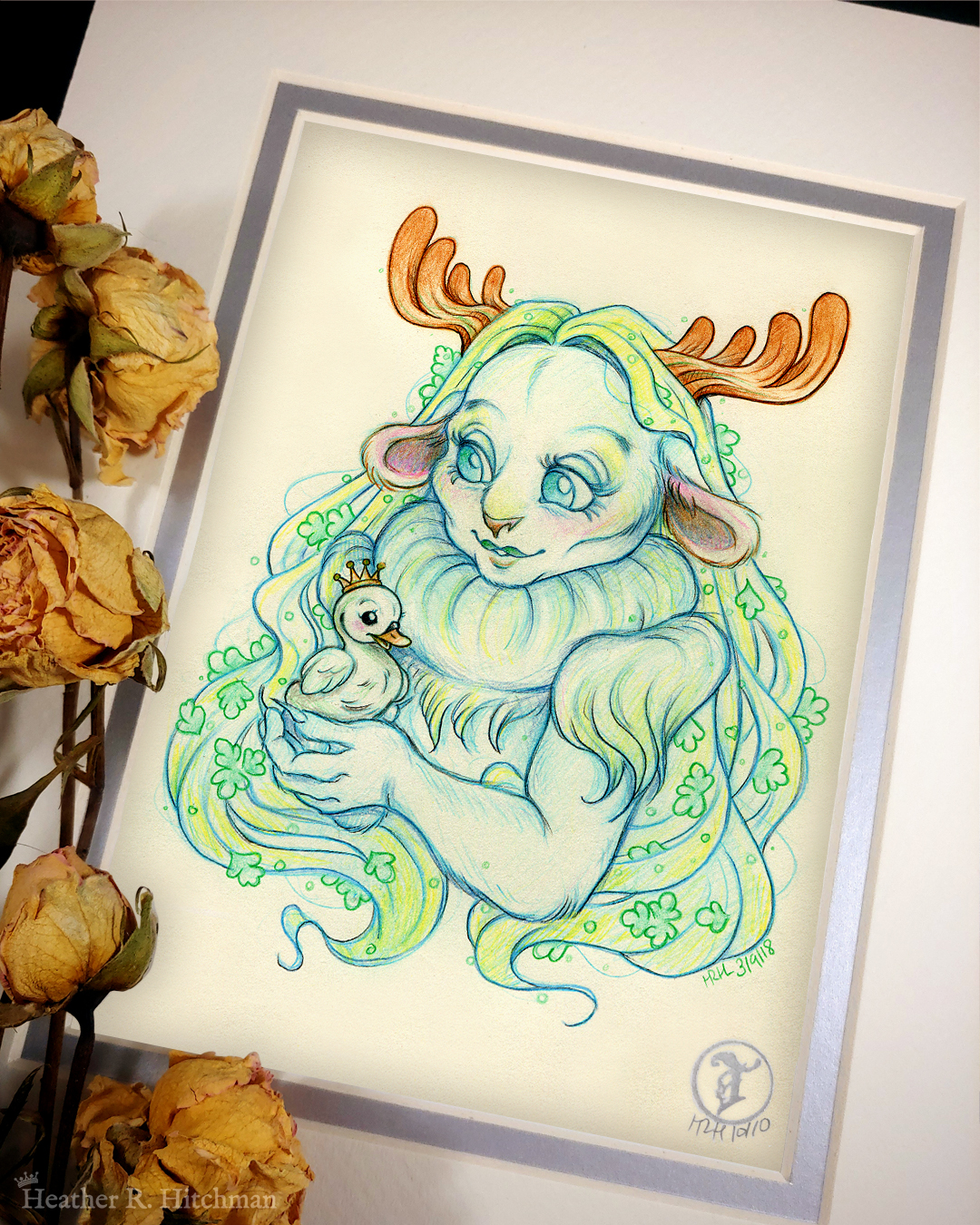 Photograph of a matted print of a graphite and colored pencil chest up portrait drawing of a child female faun with soft blueish green fur, large blue eyes, and small moose antlers. The faun’s fur is gathered into a poofy collar around her neck, creating the illusion of a ruff. The fur gathered at her shoulders looks similar to shoulder pads. She is posing at a ¾ angle to the left holding a tiny swan gosling in her hands. The gosling is wearing a tiny gold crown on its head and is looking up at the faun adoringly. The faun looks back down at the gosling, blushing with a smile on her face. Her long straight blond hair cascades around her back and shoulders, decorated with small green fern leaves. The mat-board is white on the top layer and silver on the second layer. Yellow roses rest on top of the print to the left. A small silver stamp with the Terratoff icon is at the bottom right corner of the print.