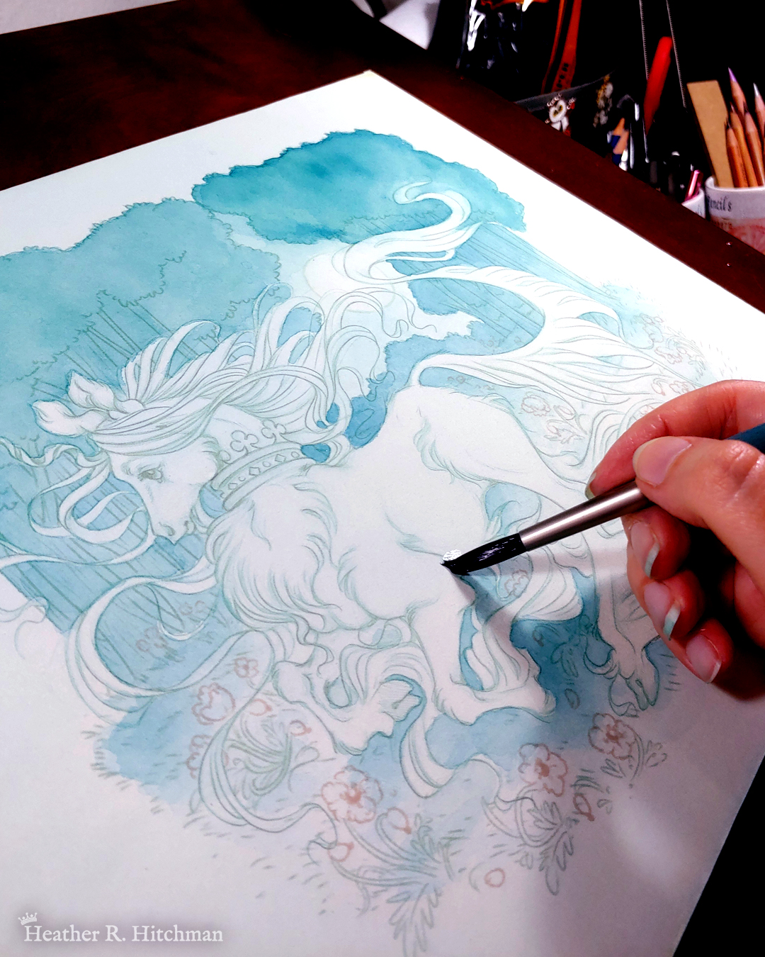 Process photograph of a full body watercolor, gouache, and colored pencil painting of a unicorn running through a moonlit forest. The artist’s hand is resting on the right section of the painting holding a wet paintbrush. The painting is very loose and sketchy with soft layers of blue watercolors and colored pencils created so far. The unicorn has long fur that flows in elegant tufts from their chest, ankles, and lion-like tail. He has a mane of long hair that swirls around in the wind behind the unicorn’s head. The unicorn has a golden horn, and wears a crown encrusted with jewels around their neck. Running in profile to the left with their front hooves close to their chest, the unicorn has a peaceful expression on its face. The background is a cool greenish blue night forest scene. In the field red poppies bloom under the unicorn’s hooves. Trees fill the far background, with an opening behind the unicorn that reveals a large full moon glowing white.