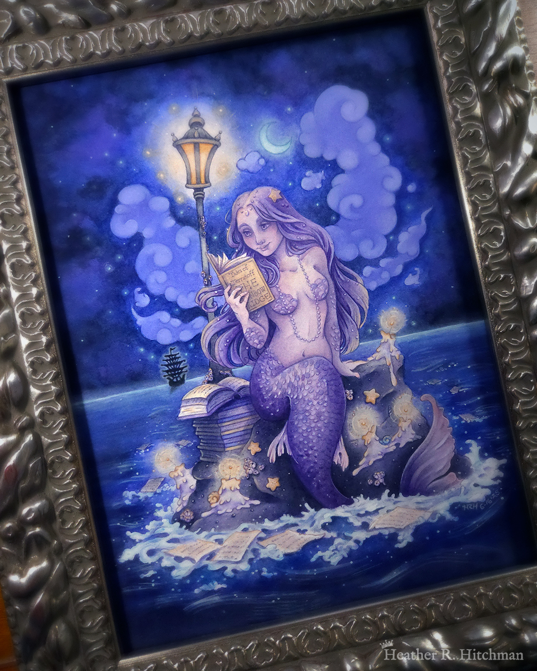 Watercolor and gouache full body painting of a purple mermaid reading a book under the moonlight while sitting on a gray rock in the middle of the sea. The rock is covered in glowing candles and also has a pile of books besides the mermaid’s tail. An old fashioned street lantern covered in barnacles is attached to the rock, illuminating orange light against a dark blue night sky. Gentle blue waves wash up against the rock. Loose white pages from books float in the water into the distance, leading towards a mysterious black ship that vanishes into the night. Puffy light blue fish shaped clouds fill the nigh sky surrounding a crescent moon. The mermaid is holding a book in her right hand up to her face. Her other hand is placed behind her as she leans back slightly, her left arm supporting her weight. Her body faces the viewer, and she has a peaceful smile as she looks towards the book and reads. The painting is in a silver ornate frame.