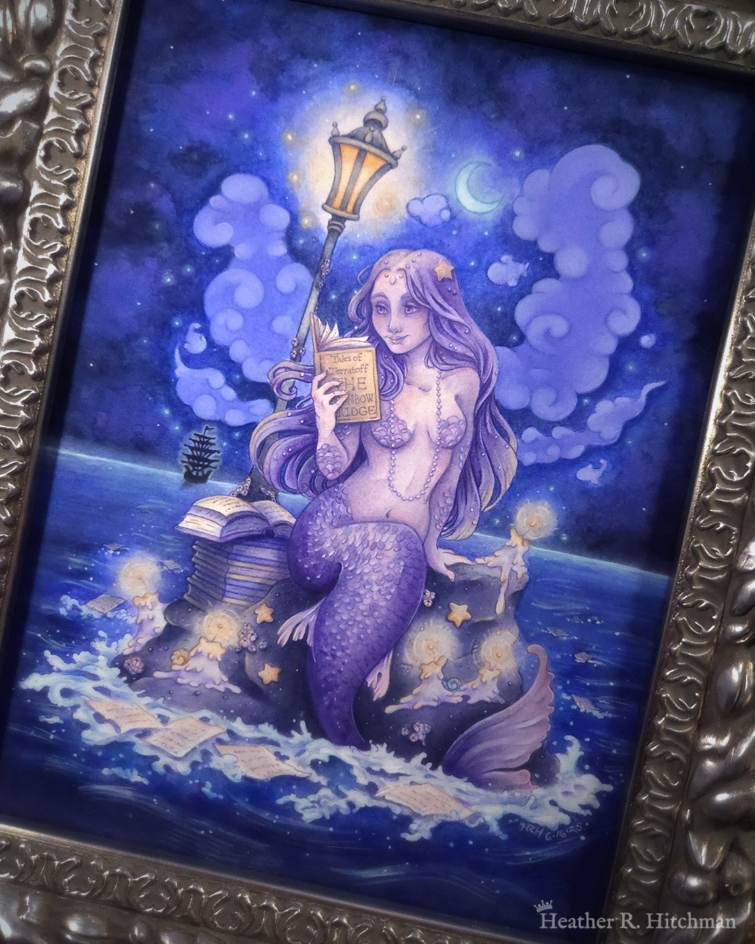 Watercolor and gouache full body painting of a purple mermaid reading a book under the moonlight while sitting on a gray rock in the middle of the sea. The rock is covered in glowing candles and also has a pile of books besides the mermaid’s tail. An old fashioned street lantern covered in barnacles is attached to the rock, illuminating orange light against a dark blue night sky. Gentle blue waves wash up against the rock. Loose white pages from books float in the water into the distance, leading towards a mysterious black ship that vanishes into the night. Puffy light blue fish shaped clouds fill the nigh sky surrounding a crescent moon. The mermaid is holding a book in her right hand up to her face. Her other hand is placed behind her as she leans back slightly, her left arm supporting her weight. Her body faces the viewer, and she has a peaceful smile as she looks towards the book and reads. The painting is in a silver ornate frame.
