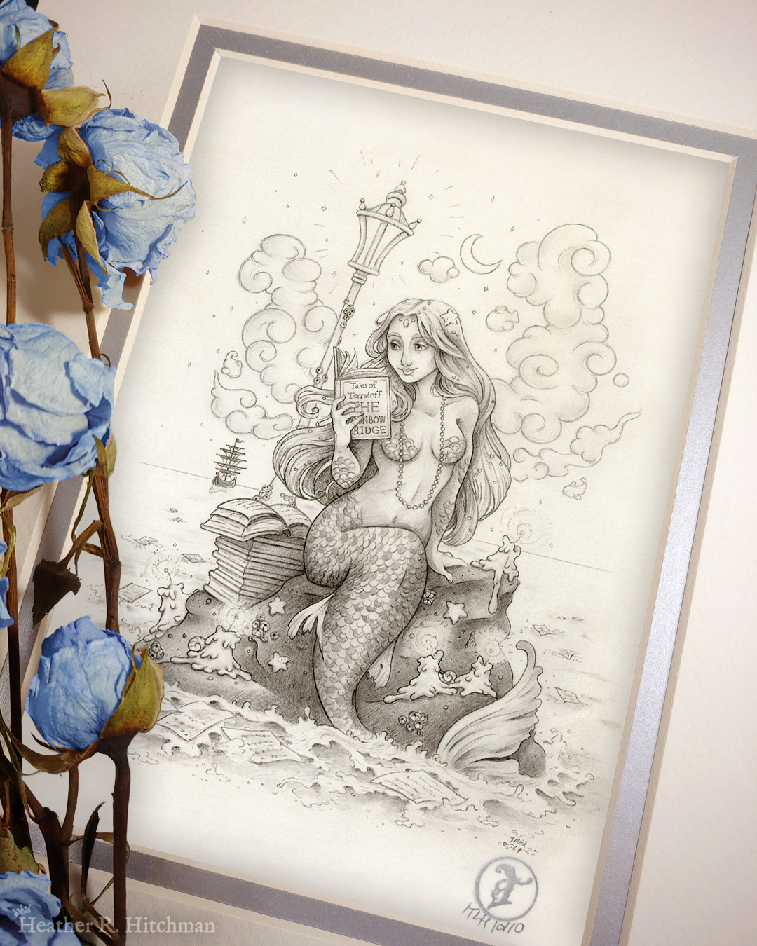 Photograph of a matted print of a black and white graphite full body drawing of a mermaid reading a book under the moonlight while sitting on a rock in the middle of the sea. The rock is covered in glowing candles and also has a pile of books besides the mermaid’s tail. An old fashioned street lantern covered in barnacles is attached to the rock, illuminating the night around the mermaid’s face. Gentle waves wash up against the rock. Loose pages from books float in the water into the distance, leading towards a mysterious ship that vanishes into the night. Puffy fish shaped clouds fill the nigh sky surrounding a crescent moon. The mermaid is holding a book in her right hand up to her face. Her other hand is placed behind her as she leans back slightly, her left arm supporting her weight. Her body faces the viewer, and she has a peaceful smile as she looks towards the book and reads. Blue roses rest on top of the print to the left. A small silver stamp with the Terratoff icon is at the bottom right corner of the print.