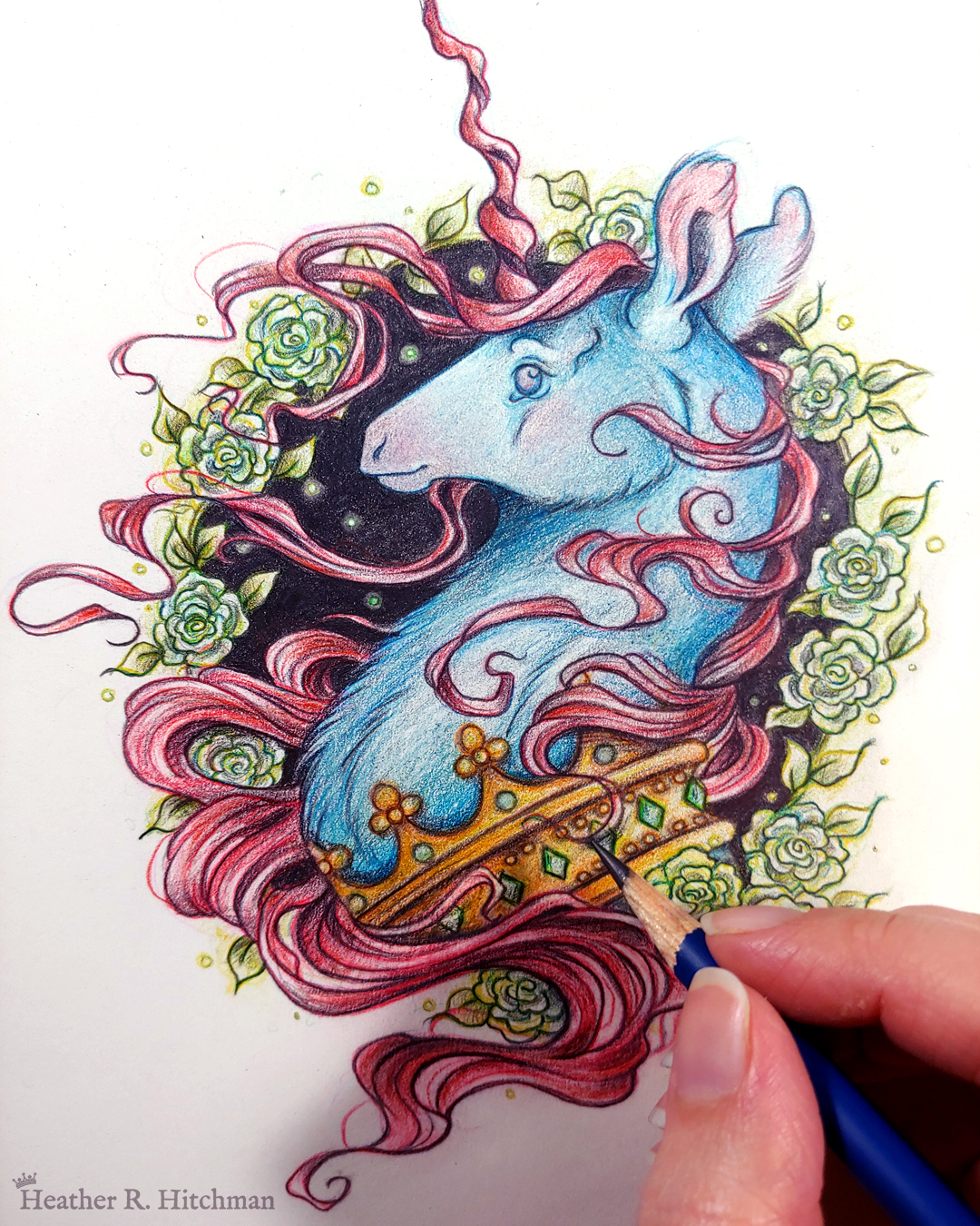 Process photograph of a graphite and colored pencil portrait drawing of a blue and red dark unicorn bust framed in a circular wreath of soft green gardenia flowers. The background inside of the wreath behind the unicorn is black with tiny orbs of green light floating around. Outside of the wreath the portrait has a sepia background color. The unicorn lifts his head proudly in profile facing to the left. He has a flowing red mane and chin beard, blue fur, and a long red corkscrew horn in the center of his forehead. The dark unicorn wears a large crown of emerald and ruby jewels around his neck. The artist’s fingertips are visible in the bottom right corner holding a graphite pencil.