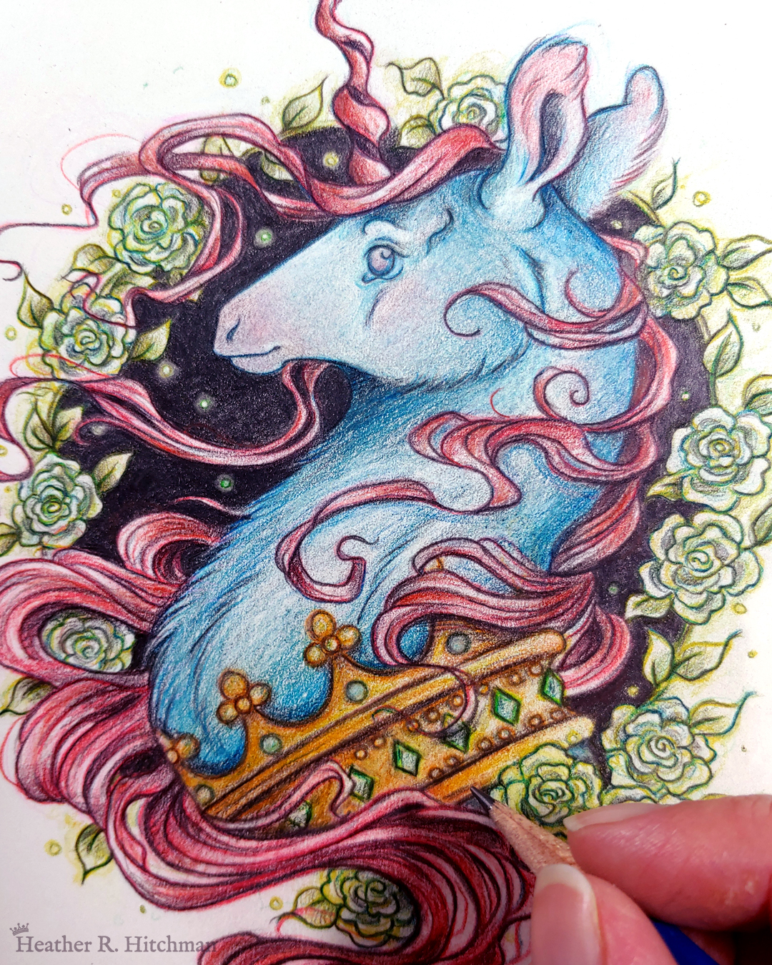 Process photograph of a graphite and colored pencil portrait drawing of a blue and red dark unicorn bust framed in a circular wreath of soft green gardenia flowers. The background inside of the wreath behind the unicorn is black with tiny orbs of green light floating around. Outside of the wreath the portrait has a sepia background color. The unicorn lifts his head proudly in profile facing to the left. He has a flowing red mane and chin beard, blue fur, and a long red corkscrew horn in the center of his forehead. The dark unicorn wears a large crown of emerald and ruby jewels around his neck. The artist’s fingertips are visible in the bottom right corner holding a graphite pencil.