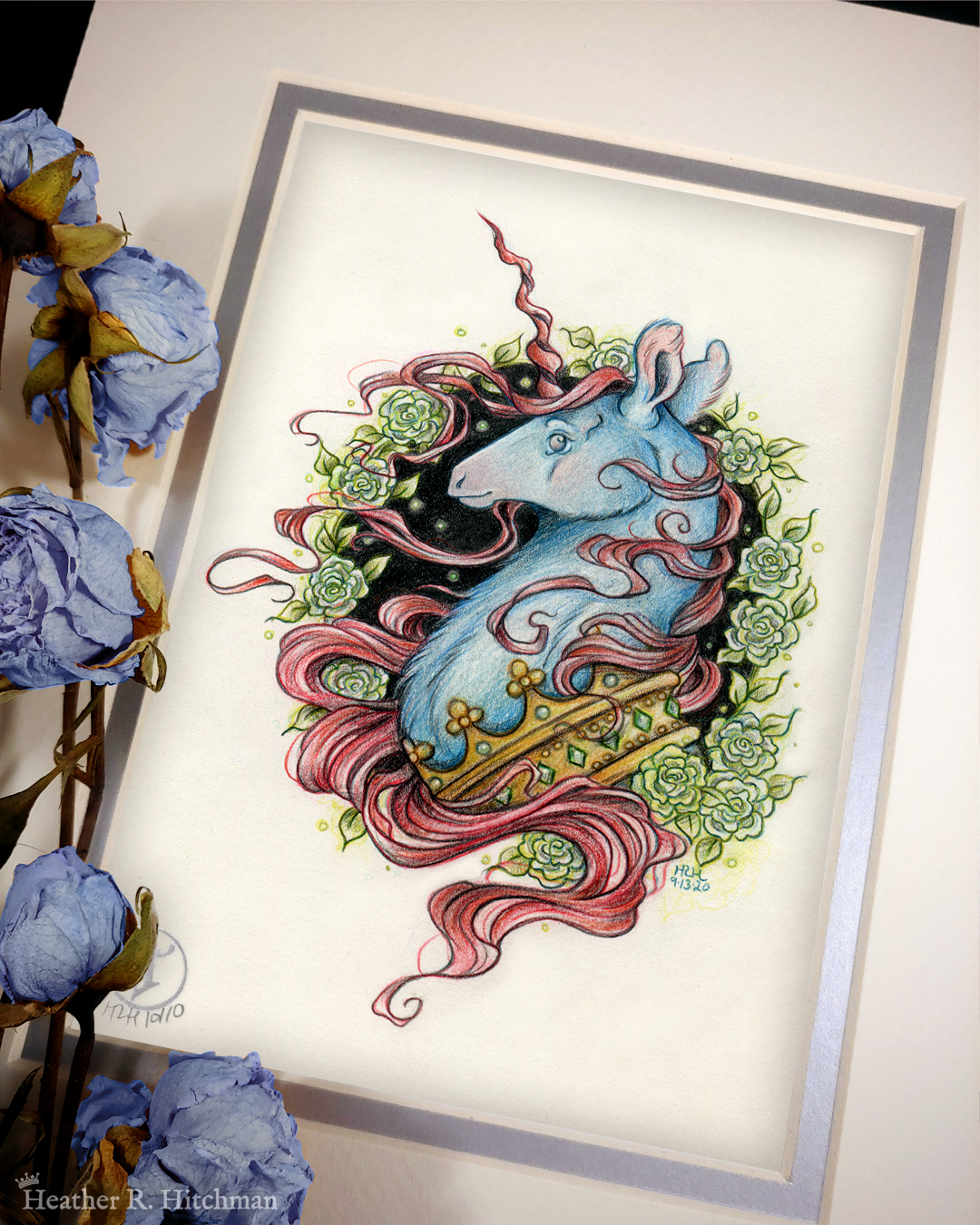 Photograph of a matted print of a graphite and colored pencil portrait drawing of a blue and red dark unicorn bust framed in a circular wreath of soft green gardenia flowers. The background inside of the wreath behind the unicorn is sepia with tiny orbs of green light floating around. Outside of the wreath the portrait has a sepia background color. The unicorn lifts his head proudly in profile facing to the left. He has a flowing red mane and chin beard, blue fur, and a long red corkscrew horn in the center of his forehead. The dark unicorn wears a large crown of emerald and ruby jewels around his neck. The mat-board is white on the top layer and silver on the second layer. Blue roses rest on top of the print to the left. A small silver stamp with the Terratoff icon is at the bottom left corner of the print, under the roses.