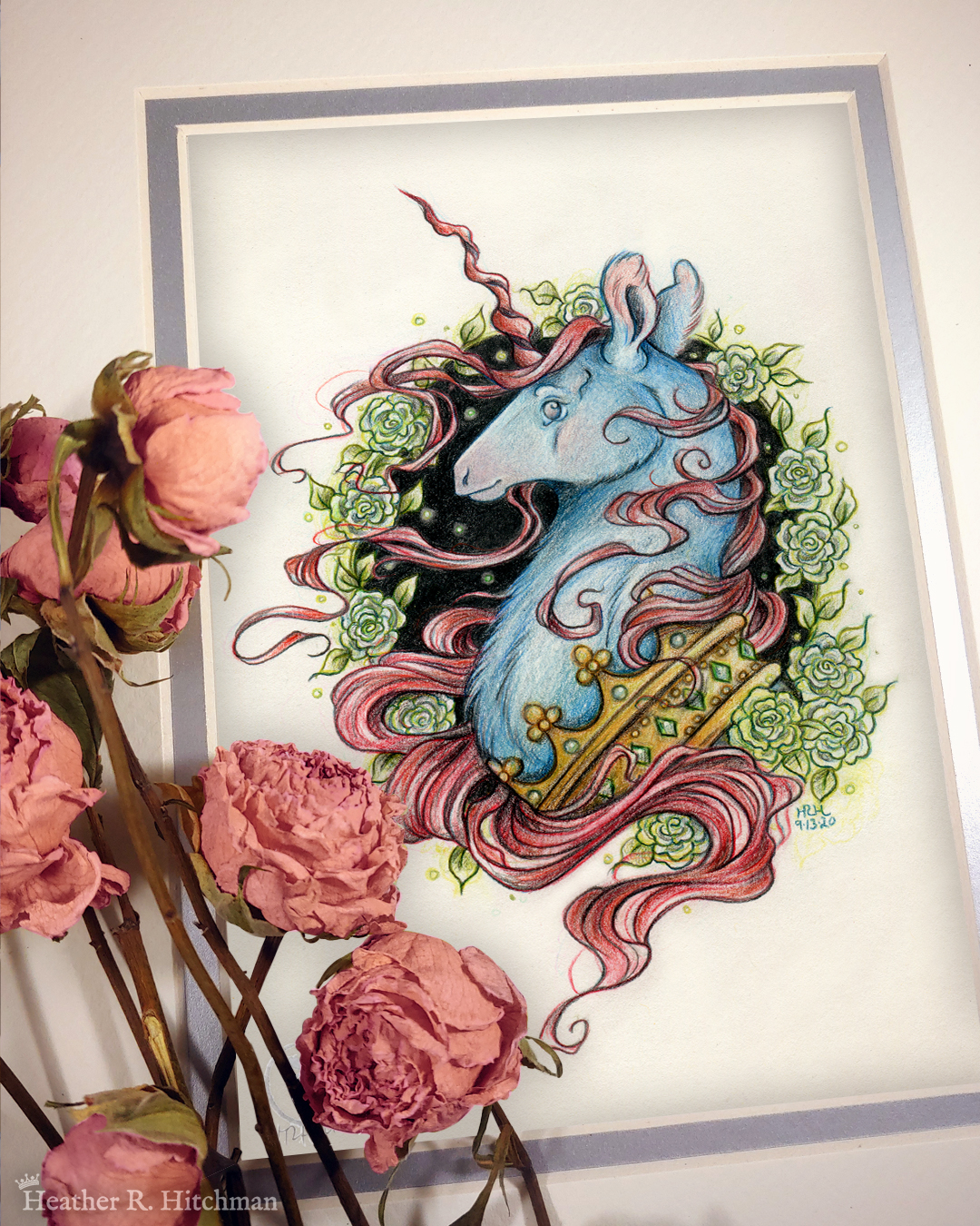 Photograph of a matted print of a graphite and colored pencil portrait drawing of a blue and red dark unicorn bust framed in a circular wreath of soft green gardenia flowers. The background inside of the wreath behind the unicorn is sepia with tiny orbs of green light floating around. Outside of the wreath the portrait has a sepia background color. The unicorn lifts his head proudly in profile facing to the left. He has a flowing red mane and chin beard, blue fur, and a long red corkscrew horn in the center of his forehead. The dark unicorn wears a large crown of emerald and ruby jewels around his neck. The mat-board is white on the top layer and silver on the second layer. Pink roses rest on top of the print to the left. A small silver stamp with the Terratoff icon is at the bottom left corner of the print, under the roses.