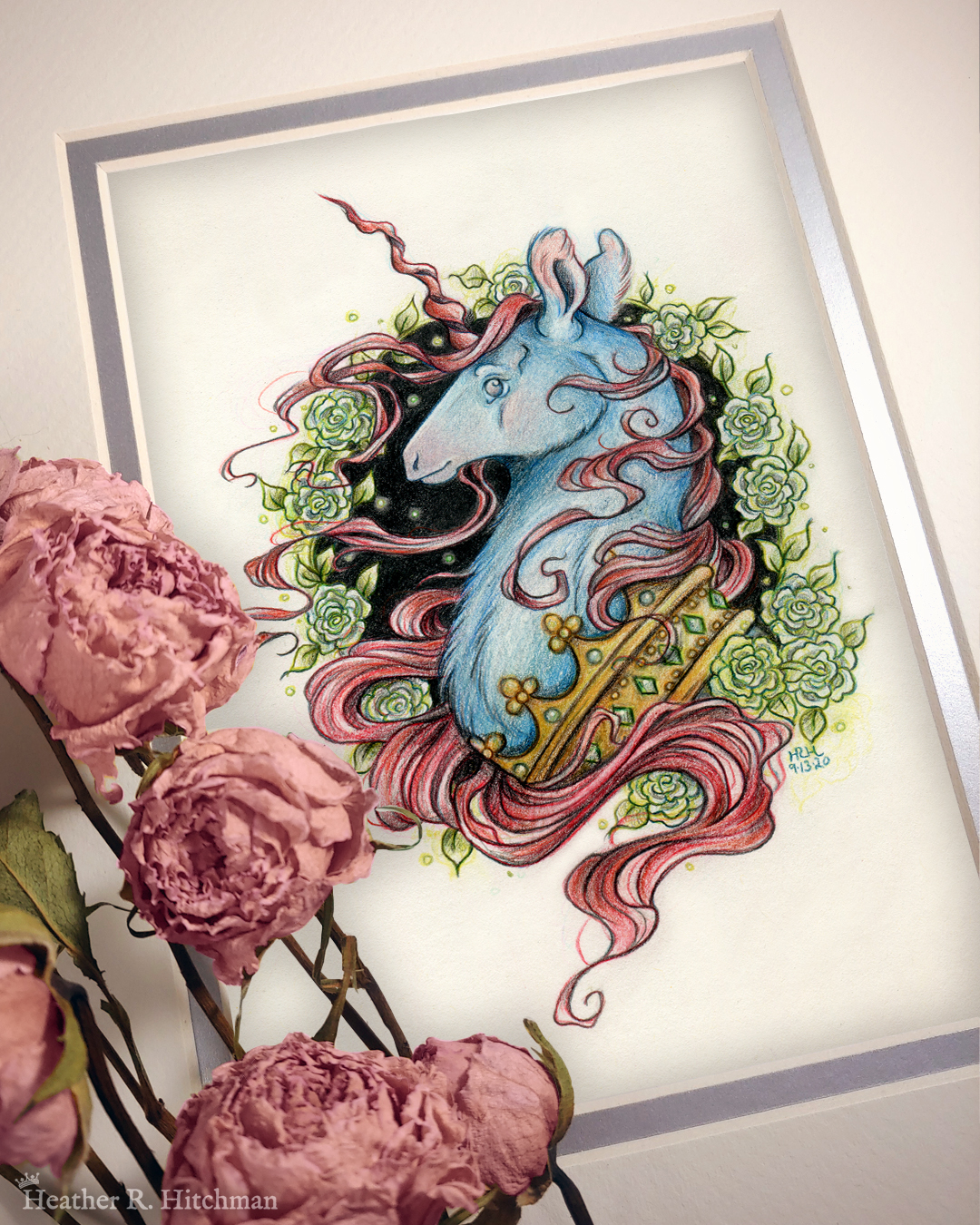 Photograph of a matted print of a graphite and colored pencil portrait drawing of a blue and red dark unicorn bust framed in a circular wreath of soft green gardenia flowers. The background inside of the wreath behind the unicorn is sepia with tiny orbs of green light floating around. Outside of the wreath the portrait has a sepia background color. The unicorn lifts his head proudly in profile facing to the left. He has a flowing red mane and chin beard, blue fur, and a long red corkscrew horn in the center of his forehead. The dark unicorn wears a large crown of emerald and ruby jewels around his neck. The mat-board is white on the top layer and silver on the second layer. Pink roses rest on top of the print to the left. A small silver stamp with the Terratoff icon is at the bottom left corner of the print, under the roses.