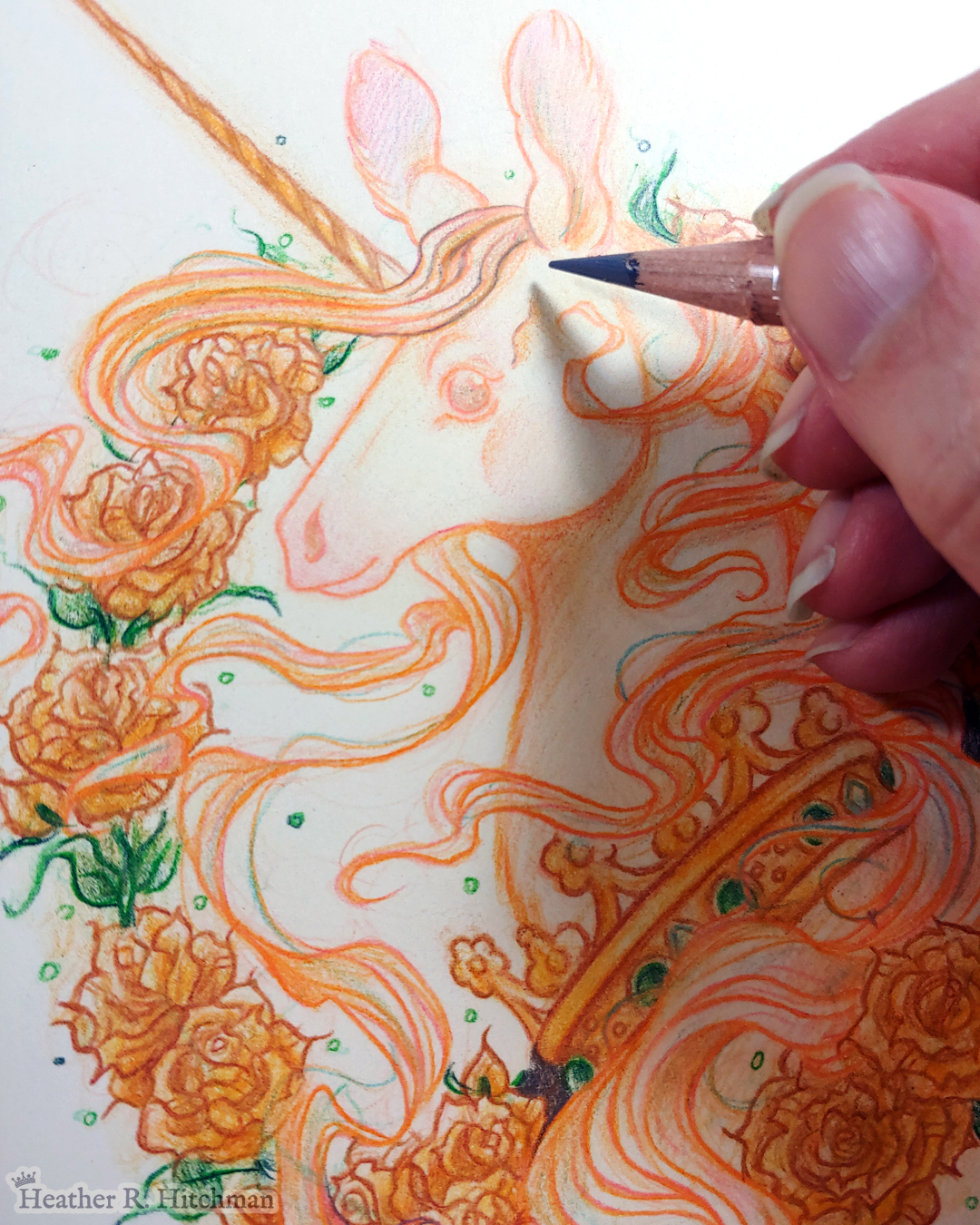 Close up process photograph of a graphite and colored pencil portrait drawing of a light gold colored royal unicorn bust framed in a circular wreath of golden roses. The background inside of the wreath behind the unicorn is white with tiny orbs of green light floating around. Outside of the wreath the portrait has a white background color. The unicorn lifts her head in profile facing to the left with a peaceful expression on her face. He has a flowing gold and pink mane and chin beard, light golden fur, and a long golden horn in the center of her forehead. The unicorn wears a large crown of green jewels around her neck. The artist’s hand holds the tip of a graphite pencil over the artwork to the top right.