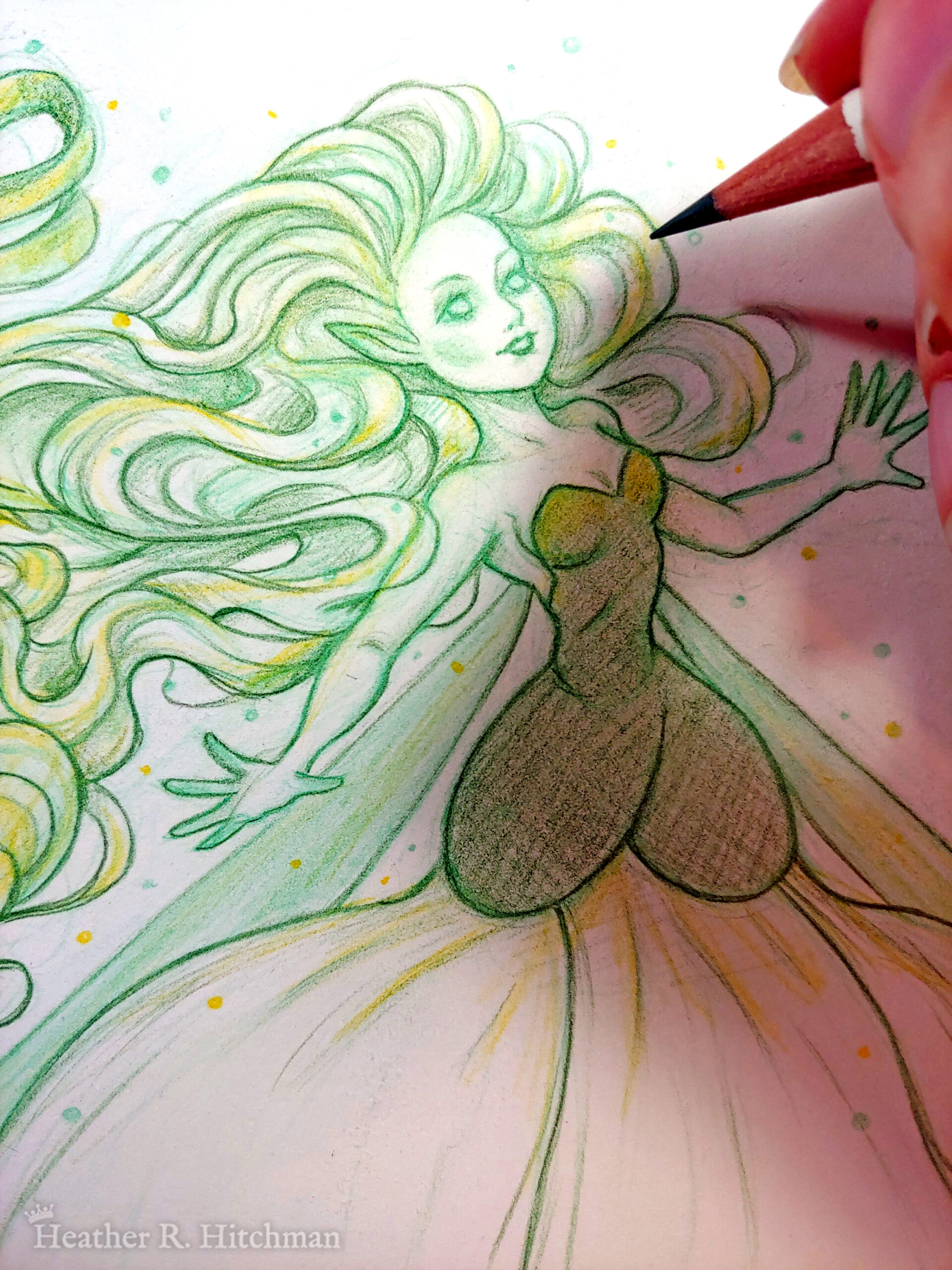 Close up process photograph of a colored pencil full body drawing of a seelie snowdrop fae. The fae faces ¾ to the right, her arms outstretched to each side and her greenish white hair billowing behind her in a heap of floating curls. The fae wears a white and green ballgown shaped like a closed upside down snowdrop blossom. She has long narrow green wings that are angled downward behind her. The fae has a round childish face, with tiny black lips and large green eyes. She looks upward and to the right with a hopeful expression on her face. The hand of the artist is to the right holding a green pencil over the image.