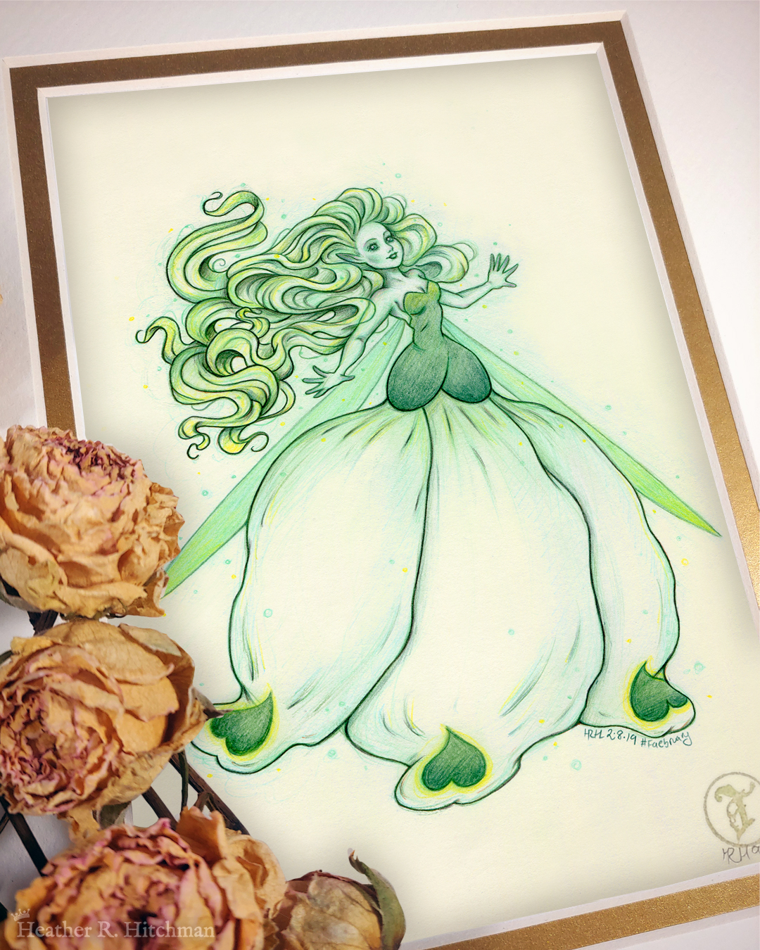 Photograph of a matted print of a colored pencil and graphite full body drawing of a seelie snowdrop fae. The fae faces ¾ to the right, her arms outstretched to each side and her greenish white hair billowing behind her in a heap of floating curls. The fae wears a white and green ballgown shaped like a closed upside down snowdrop blossom. She has long narrow green wings that are angled downward behind her. The fae has a round childish face, with tiny black lips and large green eyes. She looks upward and to the right with a hopeful expression on her face. The mat-board is white on the top layer and gold on the second layer. Yellow roses rest on top of the print to the left. A small gold stamp with the Terratoff icon is at the bottom right corner of the print.