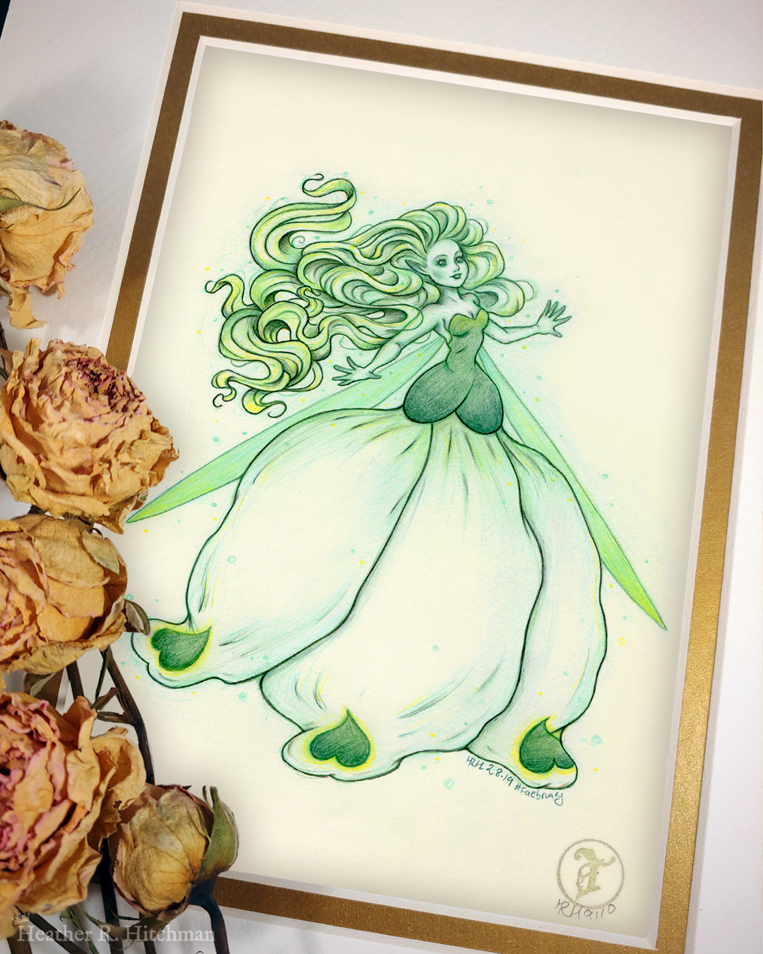 Photograph of a matted print of a colored pencil and graphite full body drawing of a seelie snowdrop fae. The fae faces ¾ to the right, her arms outstretched to each side and her greenish white hair billowing behind her in a heap of floating curls. The fae wears a white and green ballgown shaped like a closed upside down snowdrop blossom. She has long narrow green wings that are angled downward behind her. The fae has a round childish face, with tiny black lips and large green eyes. She looks upward and to the right with a hopeful expression on her face. The mat-board is white on the top layer and gold on the second layer. Yellow roses rest on top of the print to the left. A small gold stamp with the Terratoff icon is at the bottom right corner of the print.