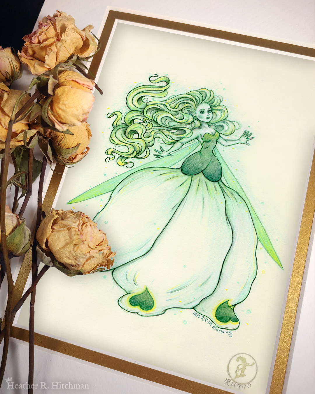 Photograph of a matted print of a colored pencil and graphite full body drawing of a seelie snowdrop fae. The fae faces ¾ to the right, her arms outstretched to each side and her greenish white hair billowing behind her in a heap of floating curls. The fae wears a white and green ballgown shaped like a closed upside down snowdrop blossom. She has long narrow green wings that are angled downward behind her. The fae has a round childish face, with tiny black lips and large green eyes. She looks upward and to the right with a hopeful expression on her face. The mat-board is white on the top layer and gold on the second layer. Yellow roses rest on top of the print to the left. A small gold stamp with the Terratoff icon is at the bottom right corner of the print.