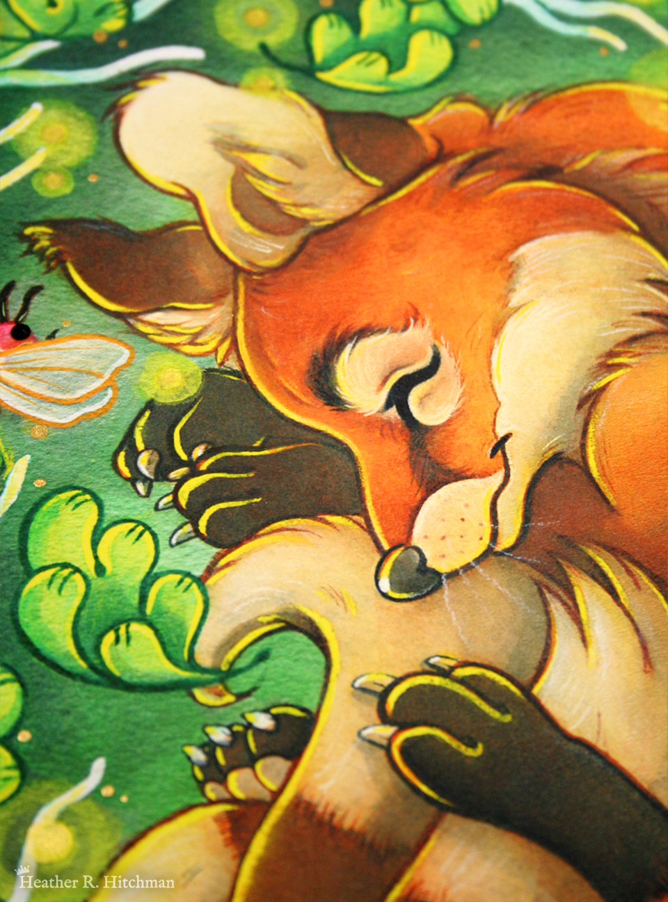 Close up photograph of a watercolor, gouache, ink, and colored pencil painting print of a sleeping fox with many tails known as a “kitsune”. The photograph focuses on the center of the artwork titled “The Dreaming Kitsune” by Heather R. Hitchman, on the kitsune’s face. The kitsune has golden orange fur, with white fur around his muzzle, eyes, and on the tips of his tails. His ears and paws have darker brown fur, and he appears to have 4 tails that are coiling around his feet. The kitsune is laying on his side with his front paws under his head like a pillow. He is coiling himself up in a cozy ball facing in profile to the left. The kitsune is sleeping with a tranquil expression on his face. He is laying on a green grass background surrounded by white branches and falling green leaves. Orbs of yellow light dance around the sleeping creature. Some of the orbs have been hand embellished by the artist with golden paint.